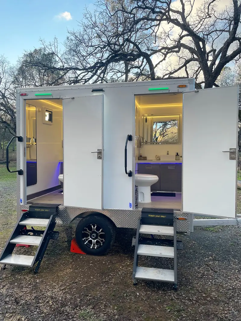 Two-stall luxury restroom trailer with interior lighting and step platforms at dusk