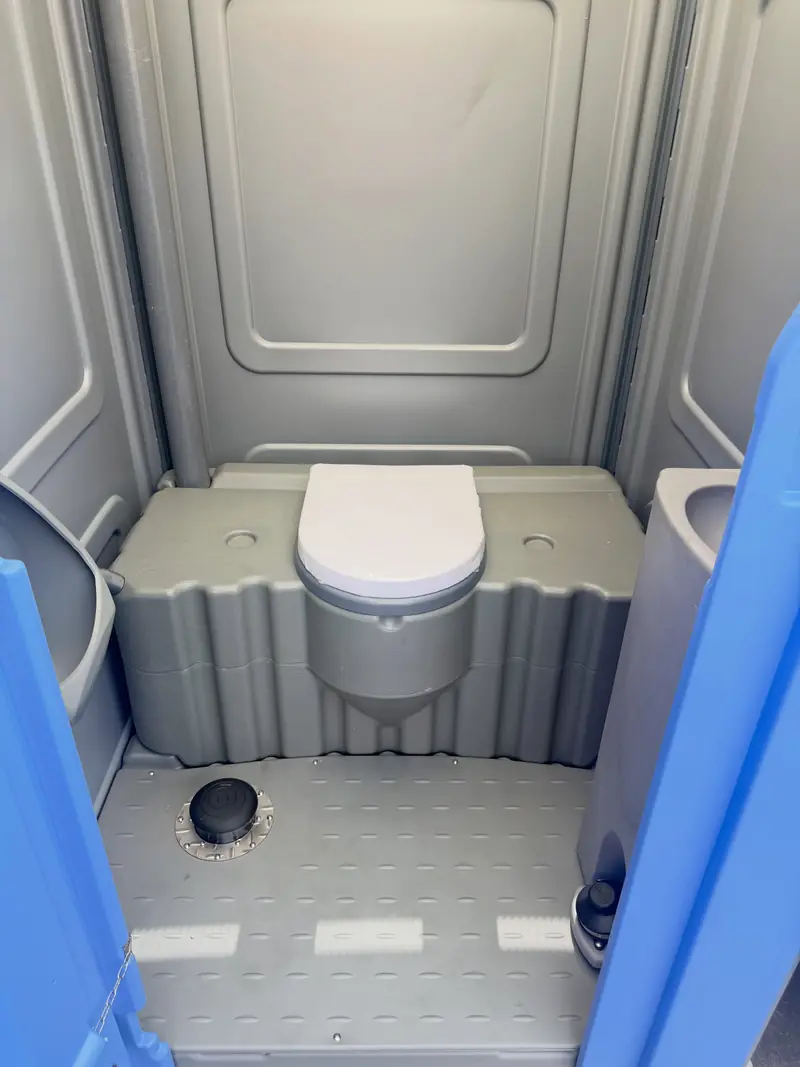 Freshly cleaned grey portable toilet interior with seat, non-slip floor and paper holder
